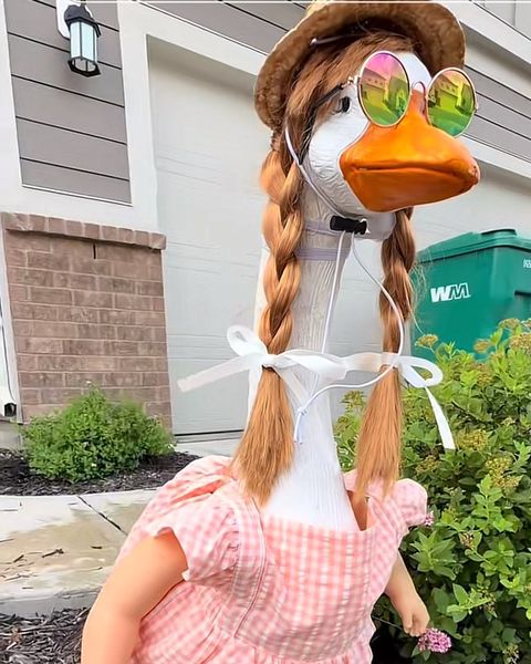 Lucy in a pink gingham dress, blonde braids, straw hat and round sunglasses